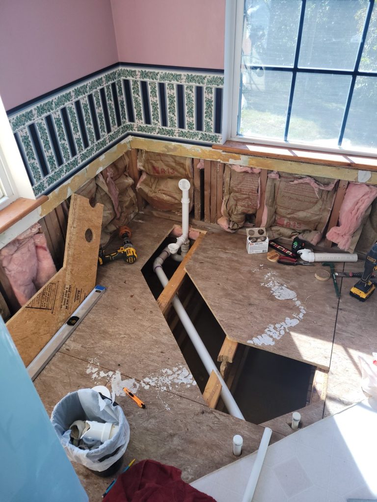 Gutted bathroom with subfloor cut open to relocate tub plumbing
